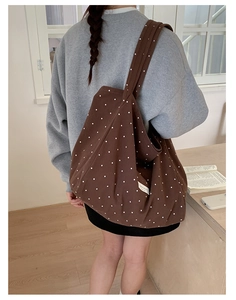 Deep brown canvas tote bag with white polka dots shown on a shoulder in a home setting
