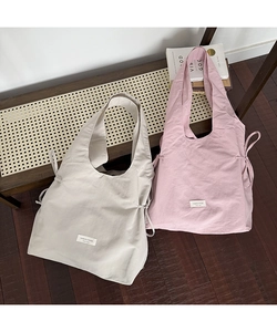 Detail of nylon tote bags with side drawstring accents and brand label on woven bench