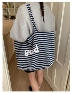 Detail shot of a large striped canvas tote bag with god lettering on a female shoulder