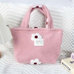 Détail d'un sac cabas en peluche rose avec broderies de fleurs blanches et étiquette