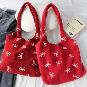Close-up of deep red felt tote bag featuring white embroidered bow patterns and soft texture