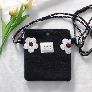 Detail of navy plush phone bag featuring white flower patches and woven rope strap