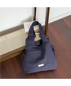 Detail view of deep blue nylon tote bag featuring side drawstring bow and white label