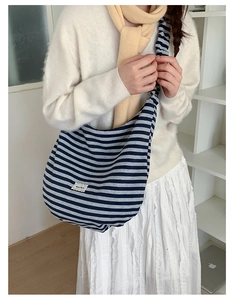 Detail view of a large blue and grey striped canvas messenger bag worn by a model