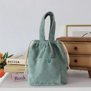 Detailed texture of green corduroy drawstring tote bag with a front snap pocket
