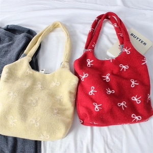 Detail of embroidered bow patterns on yellow and red felt tote bags with checkered lining