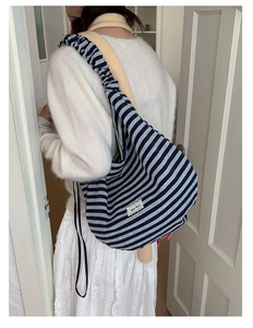 Close-up of a striped canvas tote bag with ruched shoulder strap and lace fabric label