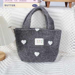 Détail d'un sac à main en peluche grise avec cœurs blancs et texture douce en polaire