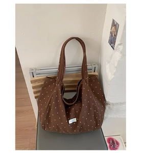 Detailed view of dark brown polka dot canvas tote bag with small woven label and shoulder straps
