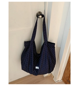 Close-up of blue polka dot canvas tote bag hanging on a door handle showing logo detail