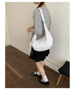 Detailed side view of a white polka dot half-moon crossbody bag on a model shoulder