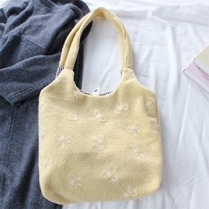 Detail of embroidered bow patterns on yellow tote bag with checkered lining and magnetic snap