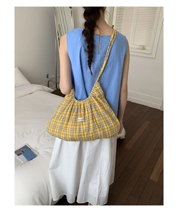 Detail of yellow plaid hobo bag with brand label worn by model in a cozy setting