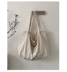 Detailed view of beige canvas tote bag with black polka dots and woven brand label