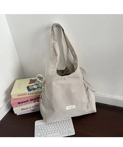 Detail view of beige nylon tote bag featuring side drawstrings and minimalist woven label