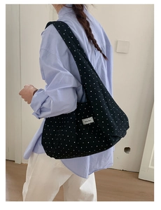 Close-up of black polka dot canvas tote bag with brand label worn on the shoulder