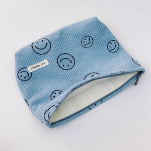 Detail view of light blue corduroy pouch featuring black smile patterns and black zipper