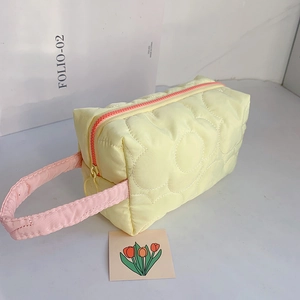 Close-up of quilted floral makeup bag with yellow fabric and pink handles and zipper