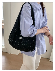 Detail of black canvas tote bag with white star pattern and brand woven label on strap
