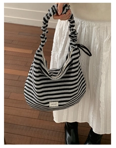 Close-up of black and grey striped knit tote bag with ruffled handle and silver zipper