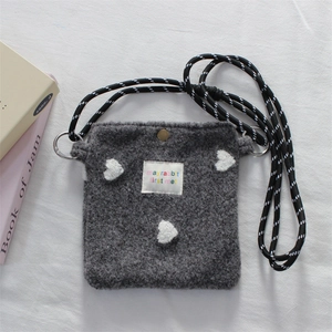 Close-up of grey plush shoulder bag with heart embroidery and braided strap detail