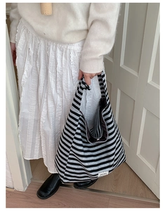 Detail of striped canvas tote bag showing large capacity and adjustable strap on a model