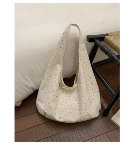 Close-up of beige canvas polka dot hobo bag with wide shoulder strap and woven chair