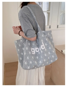 Detail of grey star-patterned tote bag with good letter print shown on model