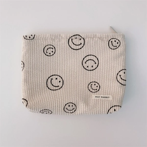 Detail of corduroy makeup bag featuring a smiley pattern and May Rabbit woven label