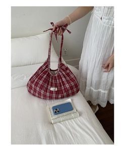 Detail of red plaid canvas tote bag featuring bow handles and a unique curved silhouette