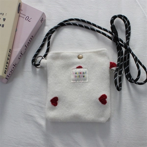 Close-up of plush cream crossbody bag with red heart appliques and striped rope strap