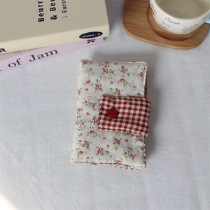 Floral handmade fabric book cover with red plaid flap and button closure on white desk