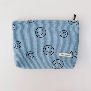 Detail of light blue corduroy makeup bag with black smiley faces and zip closure