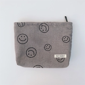 Close-up of gray corduroy makeup bag featuring black smiley prints and top zipper detail
