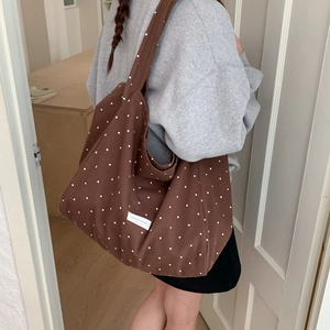 Brown polka dot canvas tote bag shown worn by a model in a minimalist indoor setting