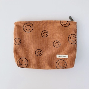 Detailed texture of brown corduroy makeup bag with smiley pattern and logo tag