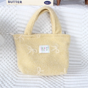 Détail du sac à main en peluche jaune avec motifs de nœuds blancs et étiquette brodée