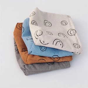Stack of four corduroy toiletry bags in white, blue, brown, and grey with smiley faces