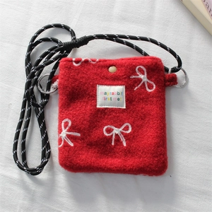 Close-up of red plush shoulder bag with white bow embroidery and woven strap details
