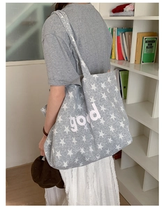 Detail of grey knitted tote bag with star print and white GOOD letter embroidery