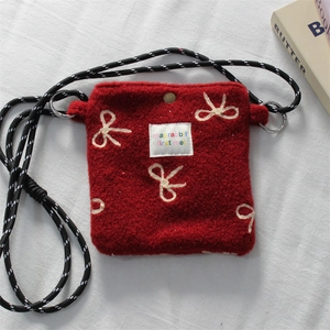Detail of red plush mini crossbody bag featuring white embroidery and metal snap button