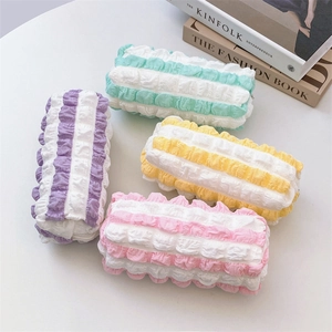 Flat lay of colorful popcorn fabric pencil cases in pastel stripes on a white desk
