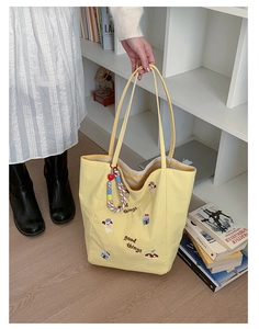 Détail du cabas en toile jaune avec broderie de dessin animé et pendentif coeur
