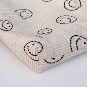 Macro shot of off-white corduroy fabric texture with minimalist black embroidered smiles
