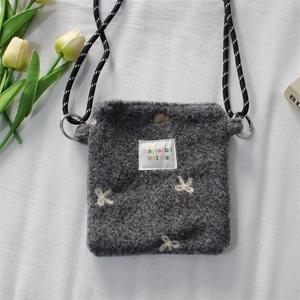 Close-up of grey plush shoulder bag featuring white bow embroidery and woven strap