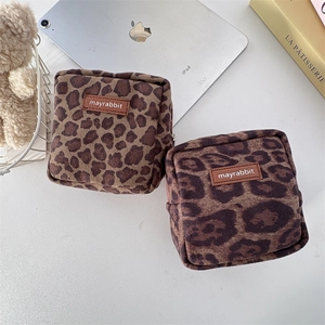 Two leopard print suede makeup bags with leather tags arranged on a desk with accessories
