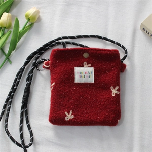 Detail of red plush mini bag with floral embroidery and woven drawstring strap