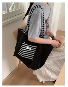 Close-up of black canvas tote bag featuring grey striped pocket and woven shoulder straps