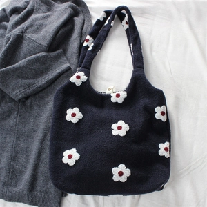 Close-up of navy knit tote bag featuring white floral embroidery on a soft fabric background