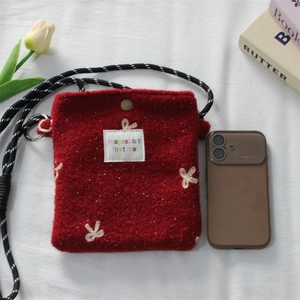 Macro detail of red plush phone bag with embroidered bow and woven shoulder strap